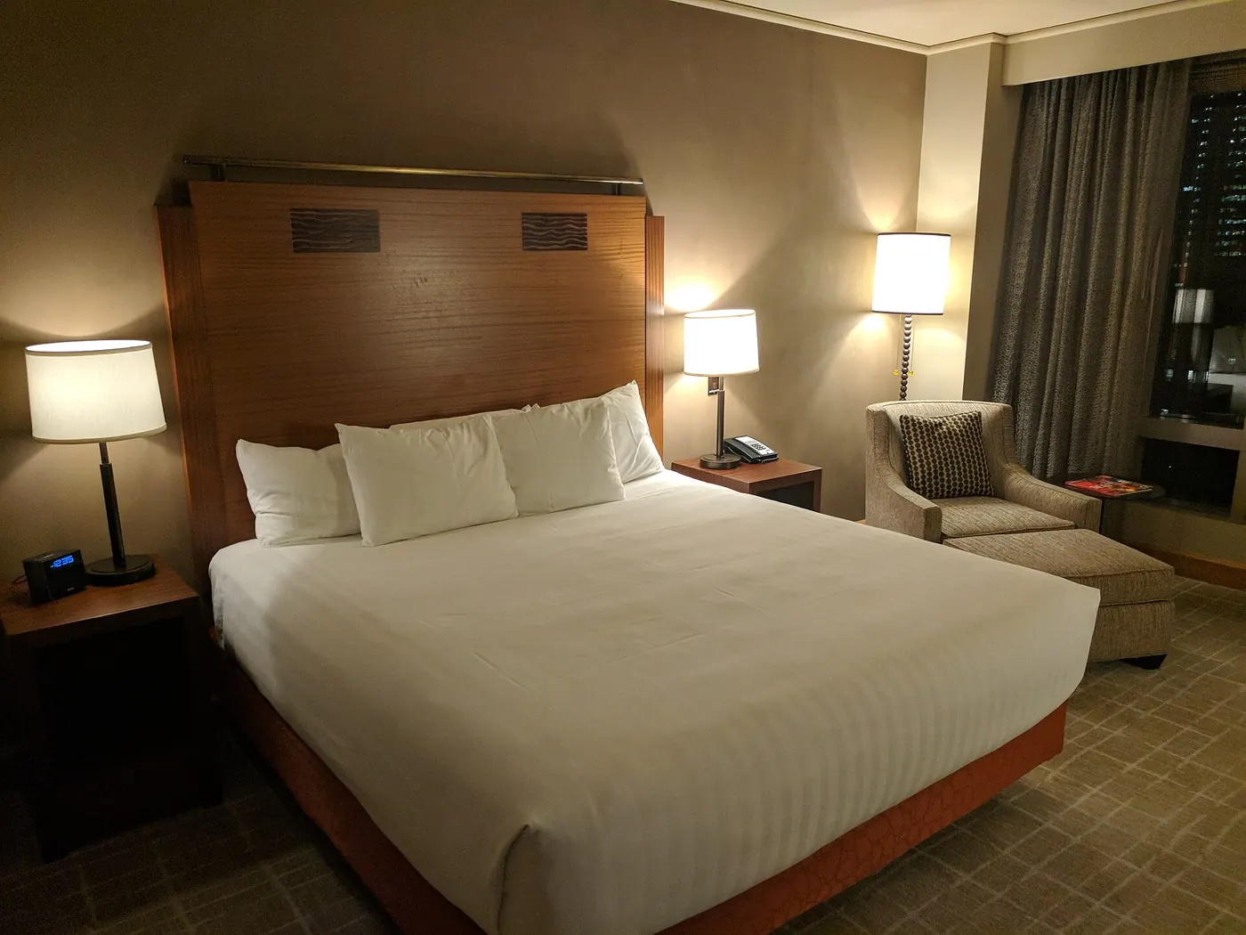 A hotel bedroom with a made bed and soft lamps