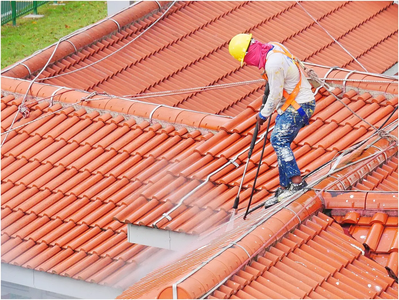 A worker cleaning a tiled roof with a pressure washer