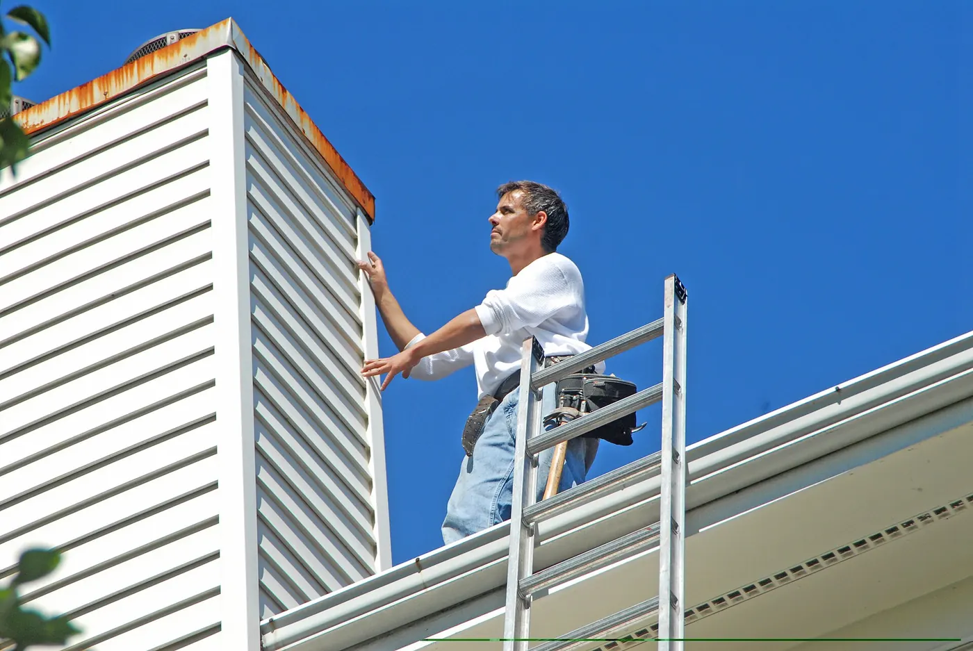 A roofer on a ladder working at the roof edge
