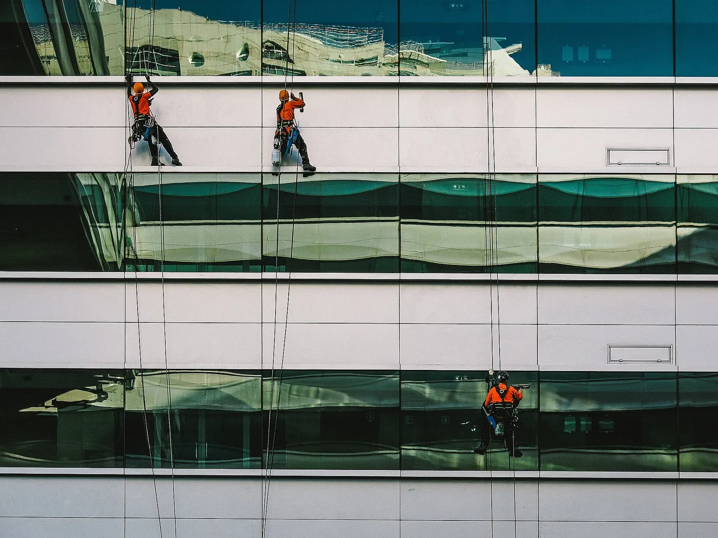 Window cleaners abseiling down a glass office building